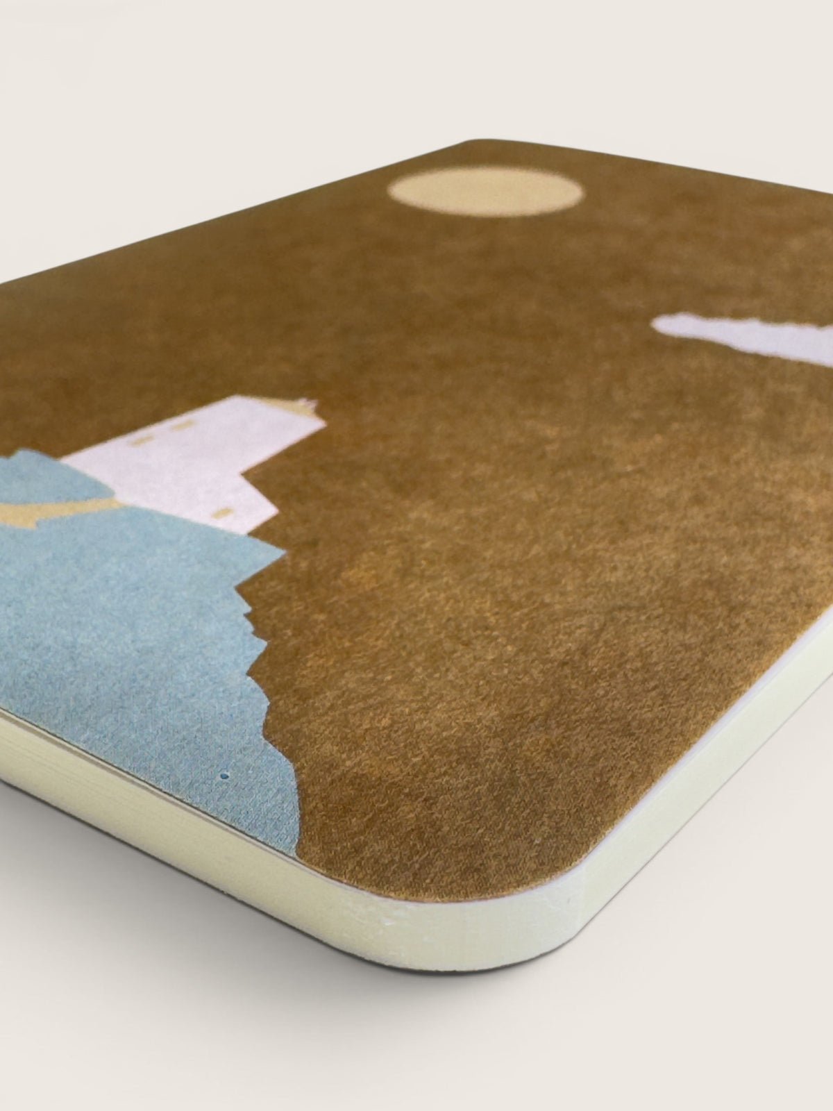Corner of an ochre waxed RO-BIKI pocket notebook, showing the mottled surface, pale printed shapes and rounded corner.