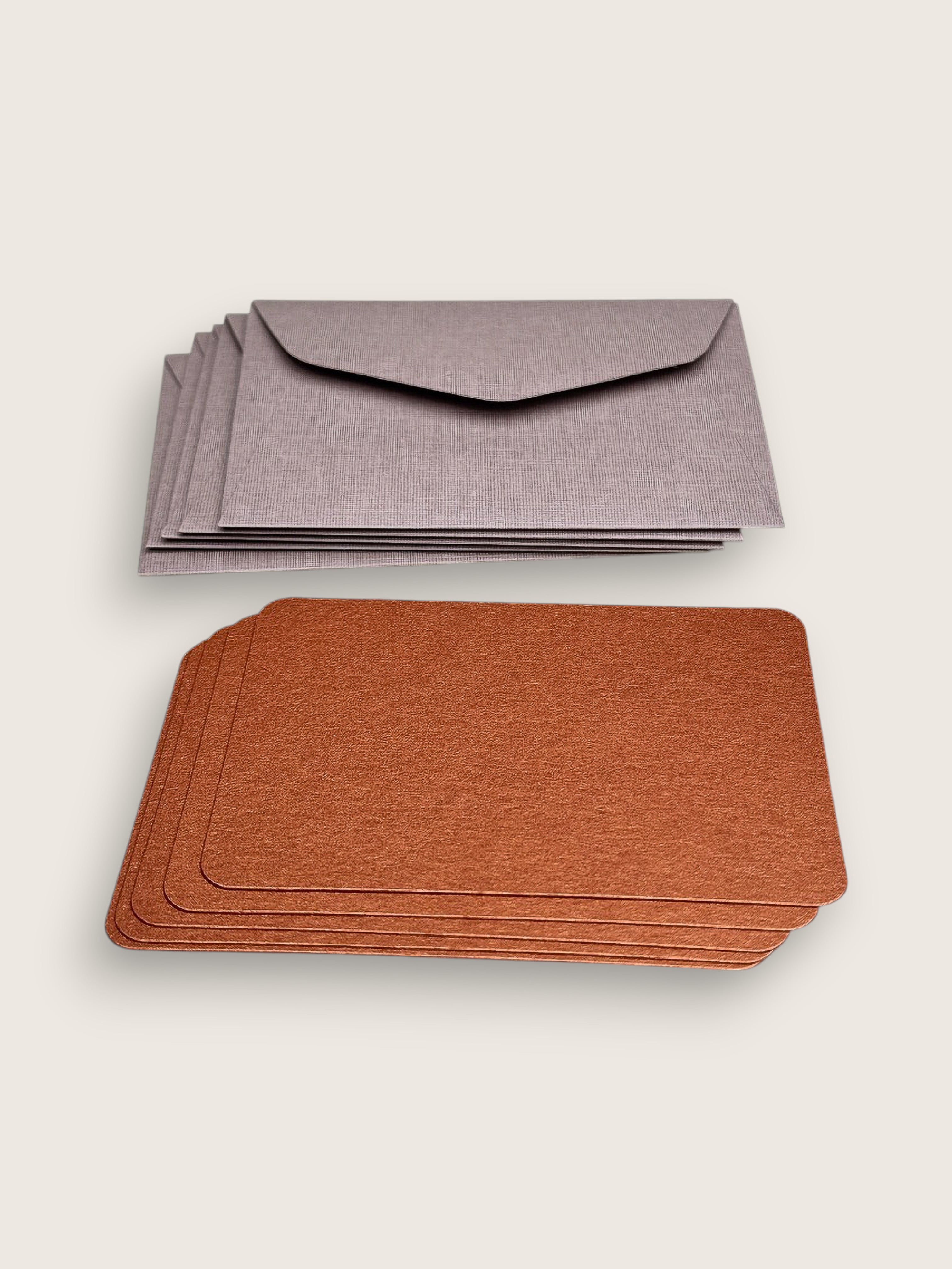 Two stacks of textured paper stationery on a light beige background: a stack of gray envelopes at the top and a stack of brown cards at the bottom.