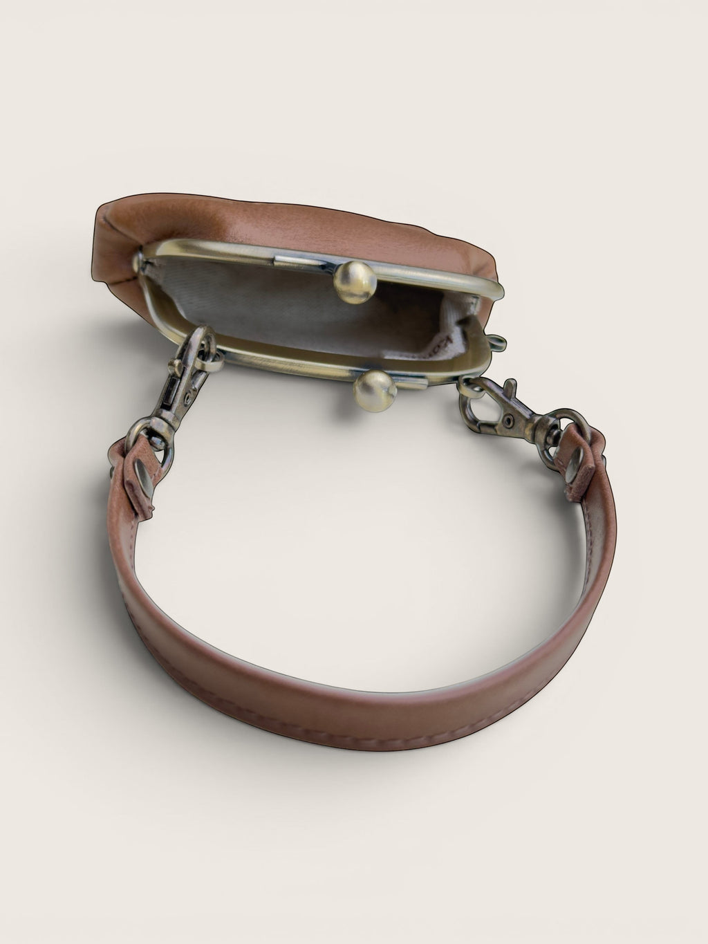 A close-up of a brown leather wristlet or clutch bag with a metal kiss-lock frame and an adjustable strap, shown on a light beige background.