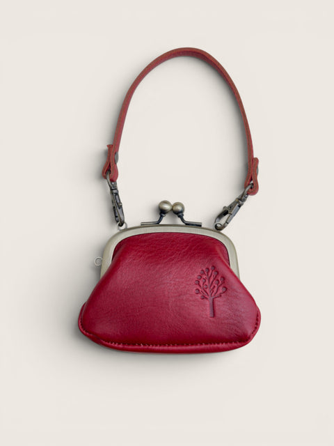 A small red leather kiss-lock coin purse with a matching red shoulder strap, silver-tone metal frame, and an embossed tree logo on the front, shown against a light beige background.