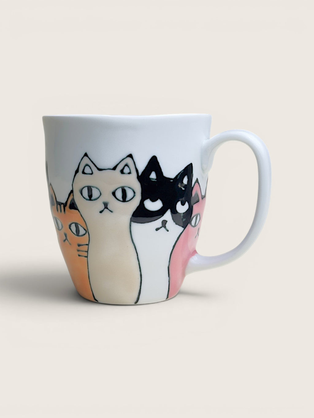 A white ceramic mug featuring a hand-drawn illustration of four cats in orange, cream, black, and pink, set against a solid light beige background.