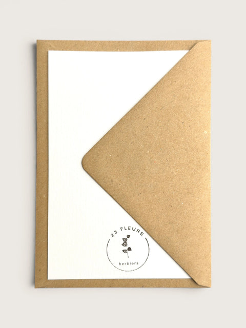 A kraft brown envelope partially covering a white card with a small circular '23 Fleurs herbiers' logo printed near the bottom.