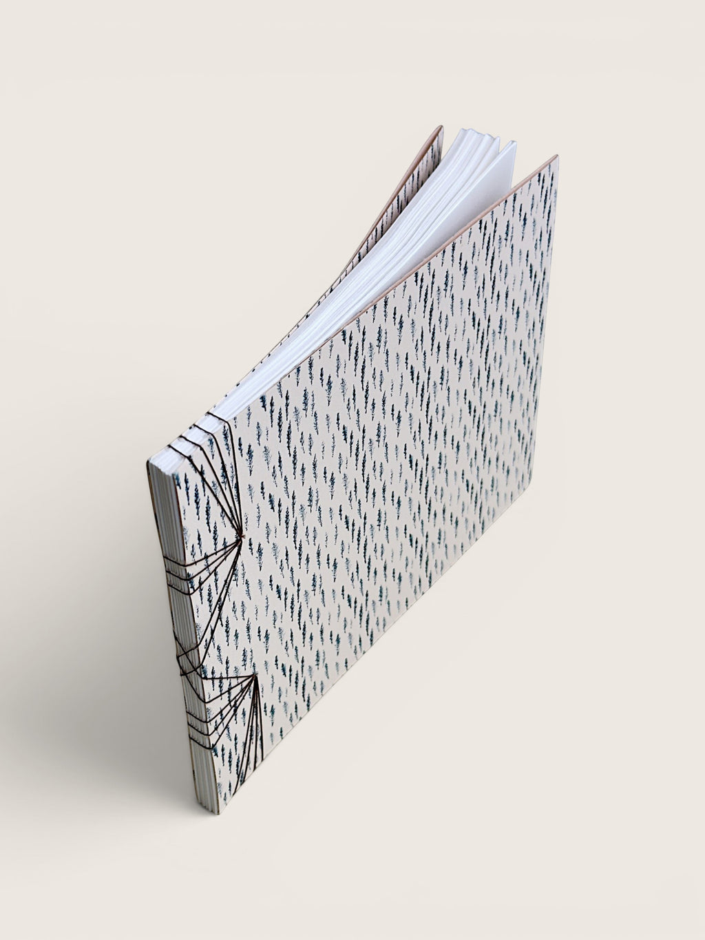 A handmade paper notebook with a black and white geometric patterned cover, standing open at an angle on a light beige background.
