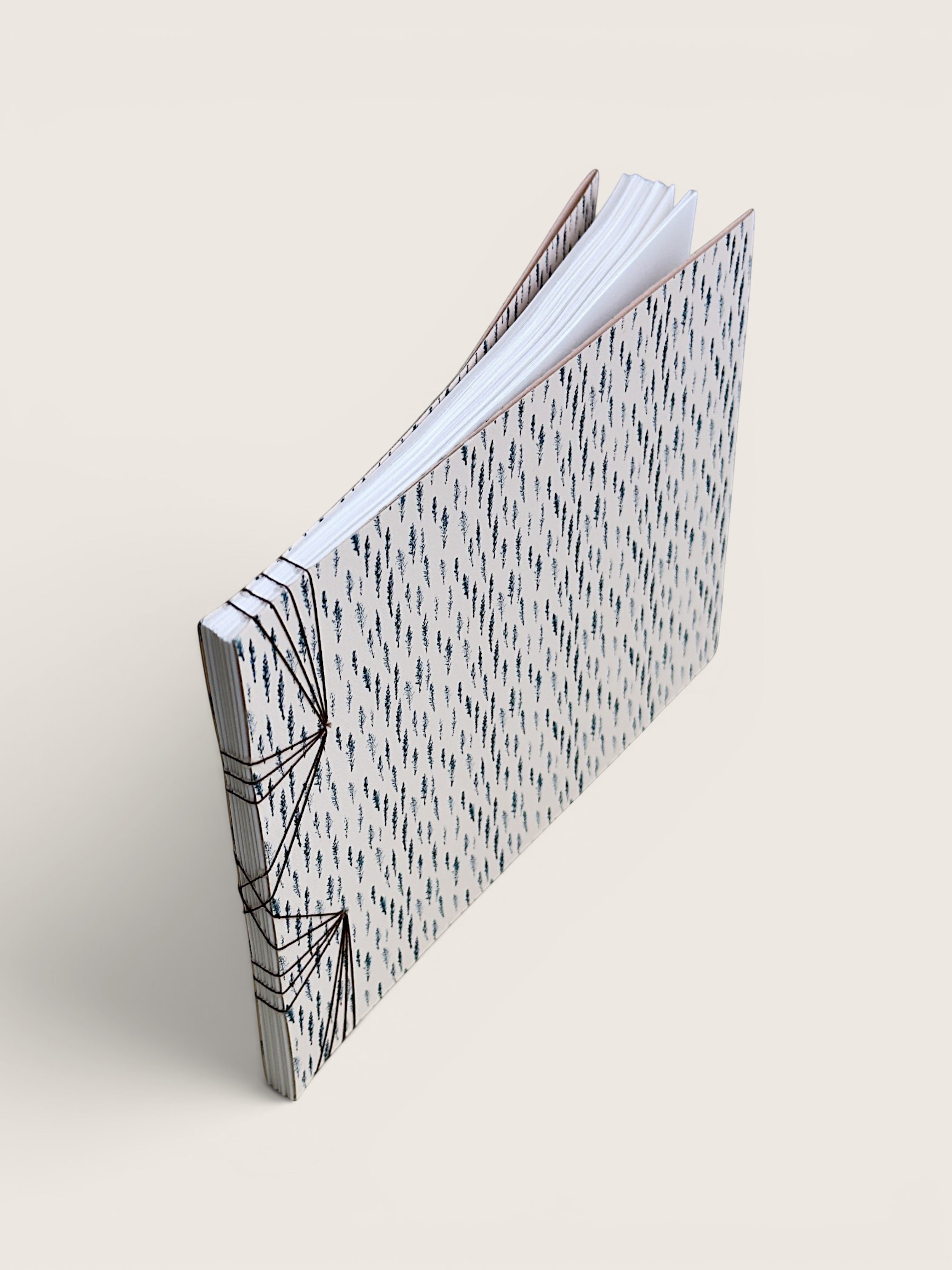 A handmade paper notebook with a black and white geometric patterned cover, standing open at an angle on a light beige background.