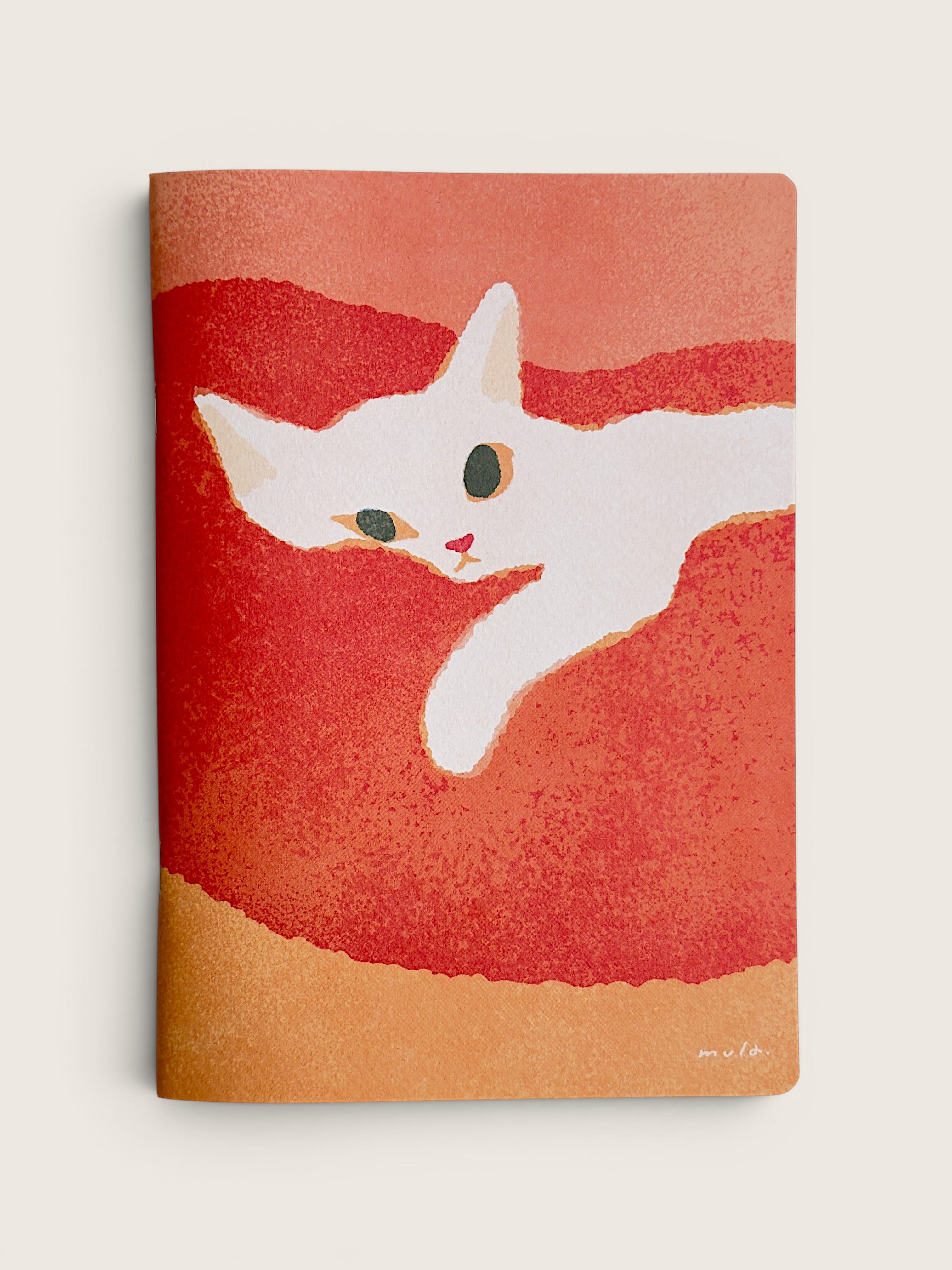 A notebook with a textured cover featuring a white cat illustration on a red and orange background, standing flat against a light beige backdrop.
