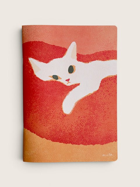 A notebook with a textured cover featuring a white cat illustration on a red and orange background, standing flat against a light beige backdrop.