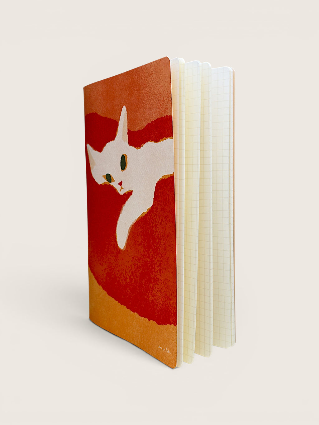 A notebook with a textured cover featuring a white cat illustration on a red and orange background, standing upright against a light beige backdrop.