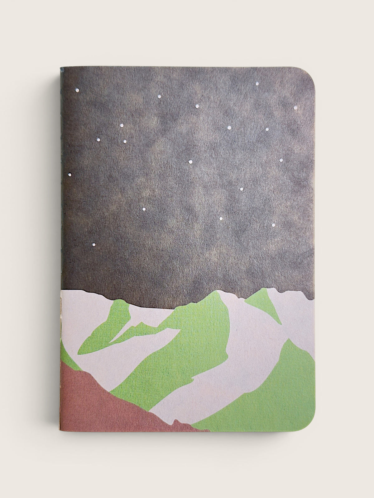 A hardcover notebook with a minimalist mountain and starry night design on the cover, shown against a light beige background.