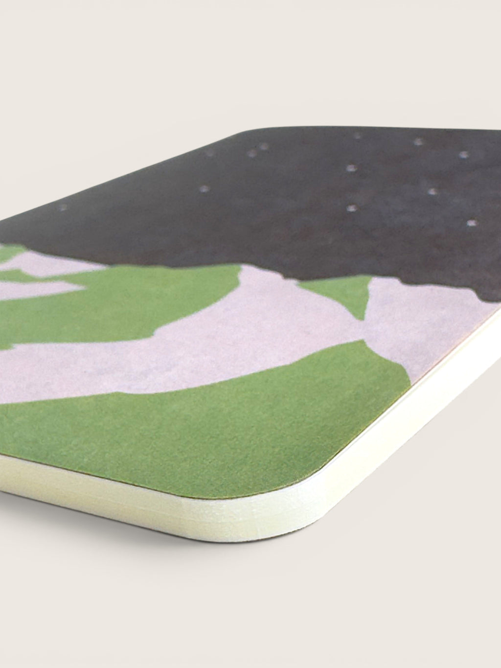 A close-up of a rectangular product with rounded corners, featuring an abstract landscape-style print in green, pale pink, and dark charcoal, with a light beige edge visible along the bottom.