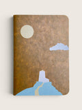 A notebook with a textured brown cover featuring a minimalist illustration of a lighthouse on a blue hill under a cream moon and light blue cloud, shown on a light beige background.