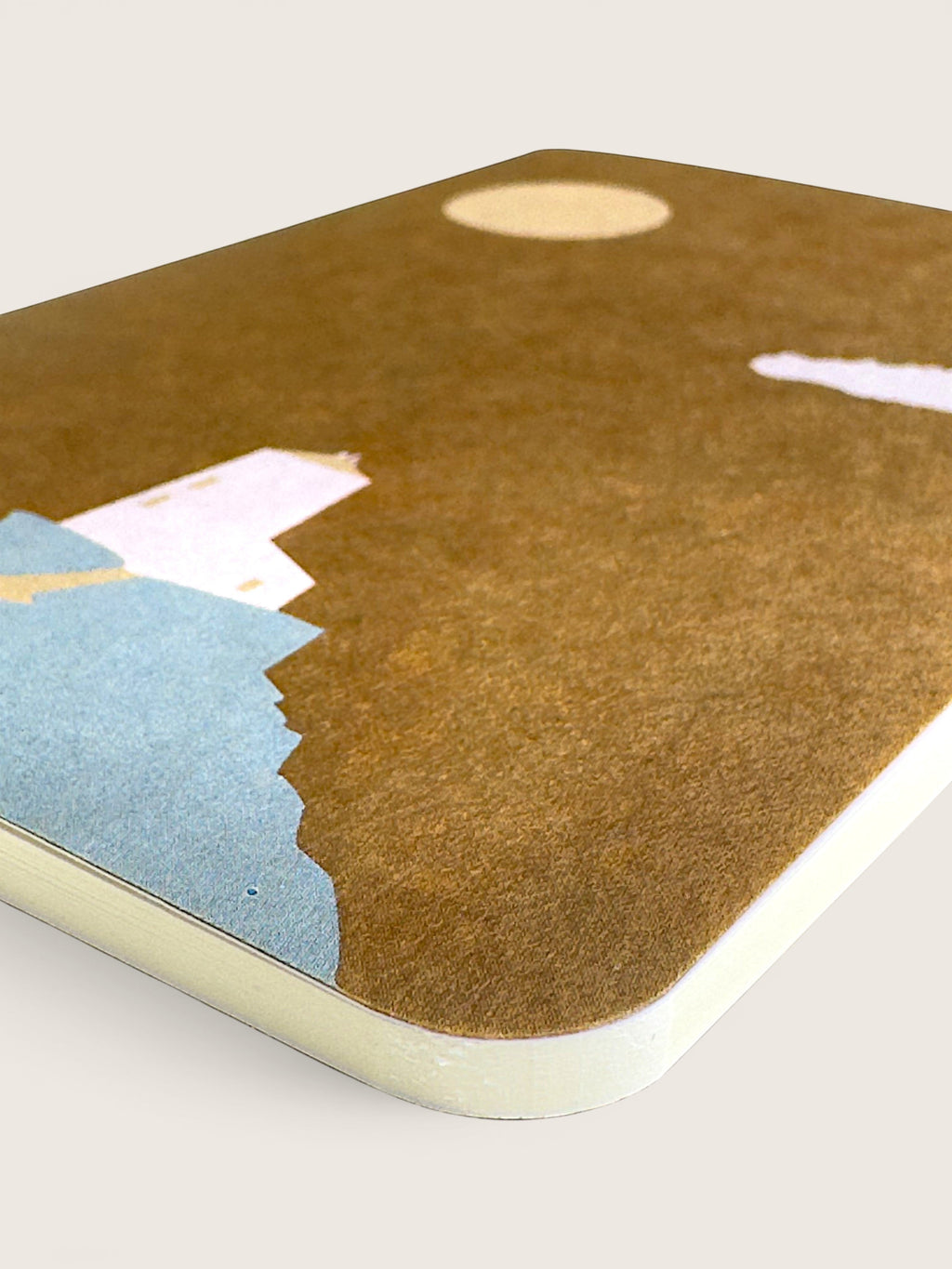 A close-up of a rectangular desk mat or mousepad with rounded corners, featuring a textured brown background with abstract paper cutouts in light blue, pale pink, cream, and gold. The product is shown at an angle on a light beige background.