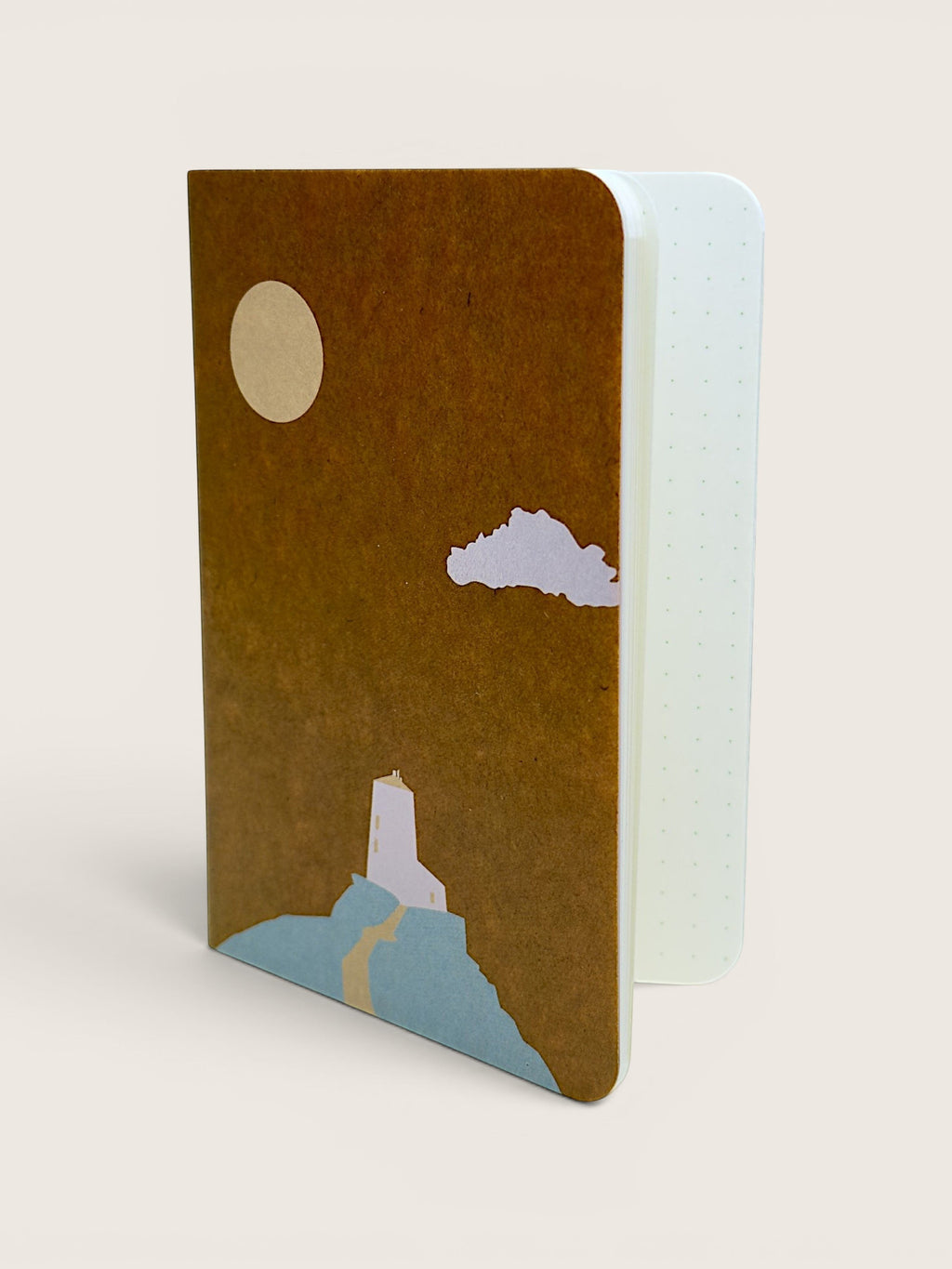 A notebook with a textured brown cover featuring a minimalist illustration of a cream sun, white cloud, and light blue landscape, shown standing open against a light beige background.
