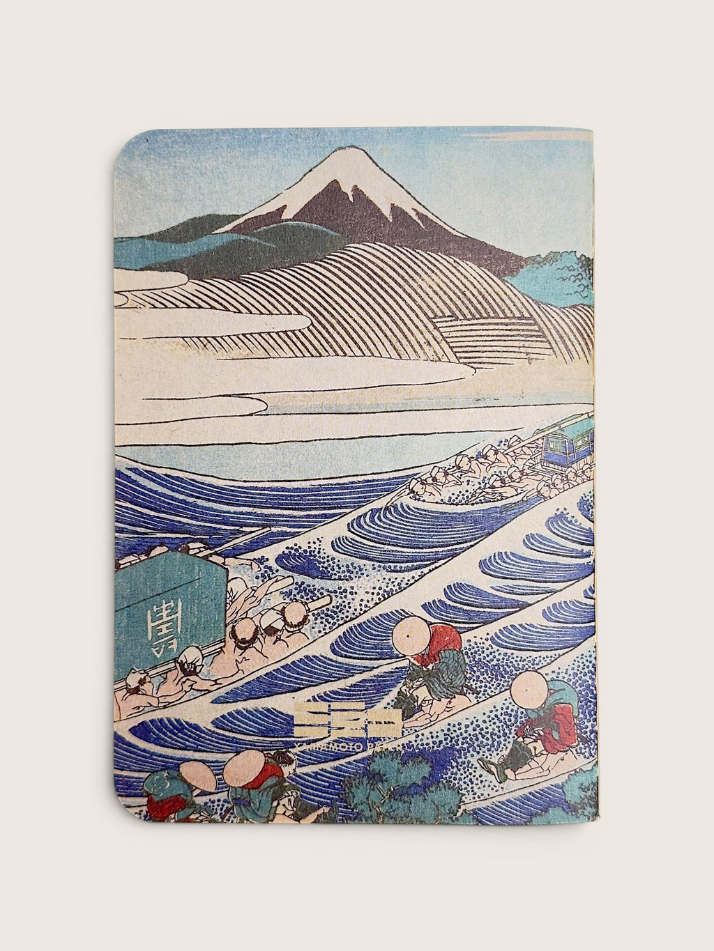 A notebook featuring a classic Japanese ukiyo-e woodblock print of Mount Fuji and waves, with rowing figures in the foreground, shown on a light beige background.
