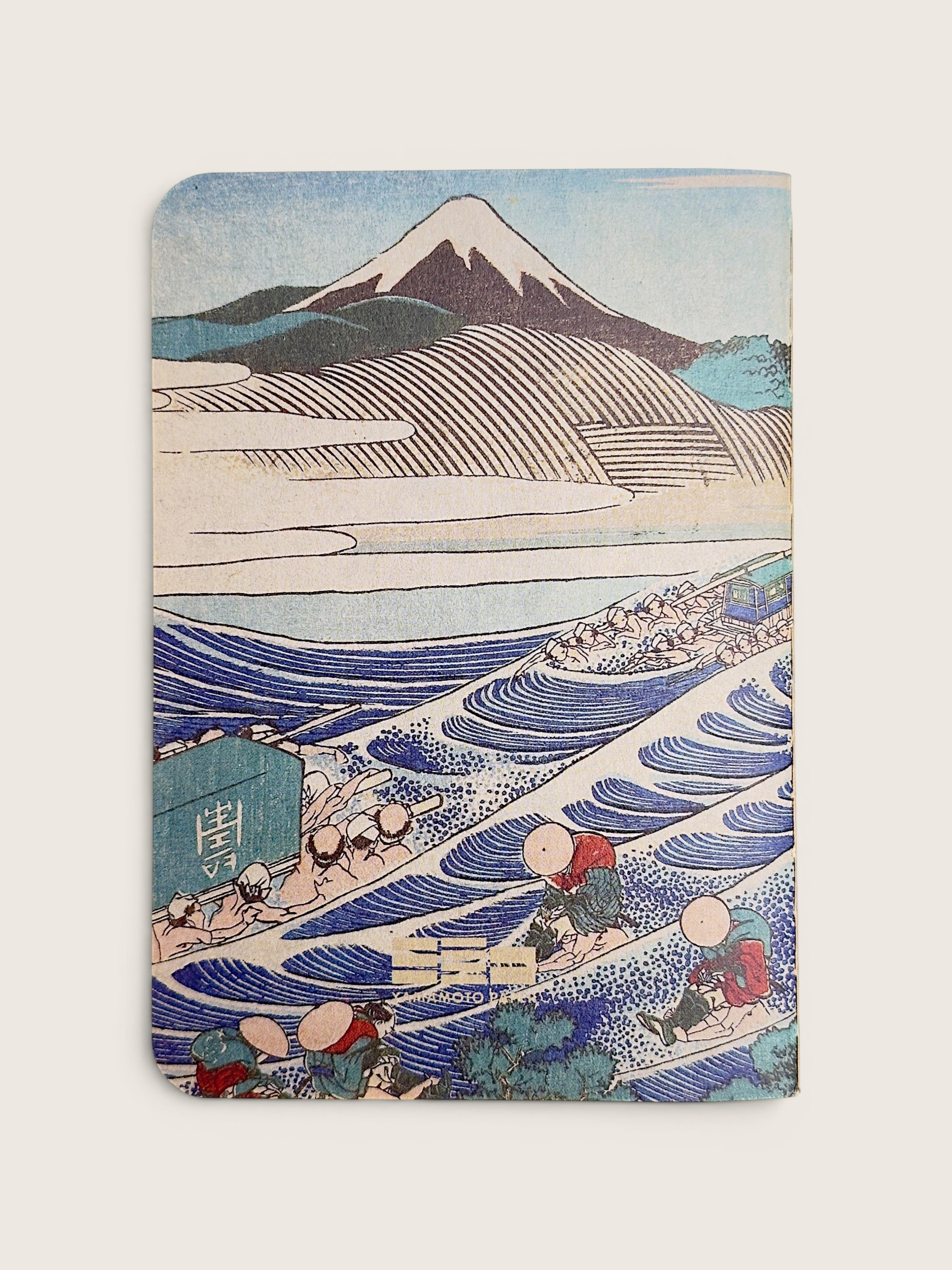 A notebook featuring a classic Japanese ukiyo-e woodblock print of Mount Fuji and waves, with rowing figures in the foreground, shown on a light beige background.