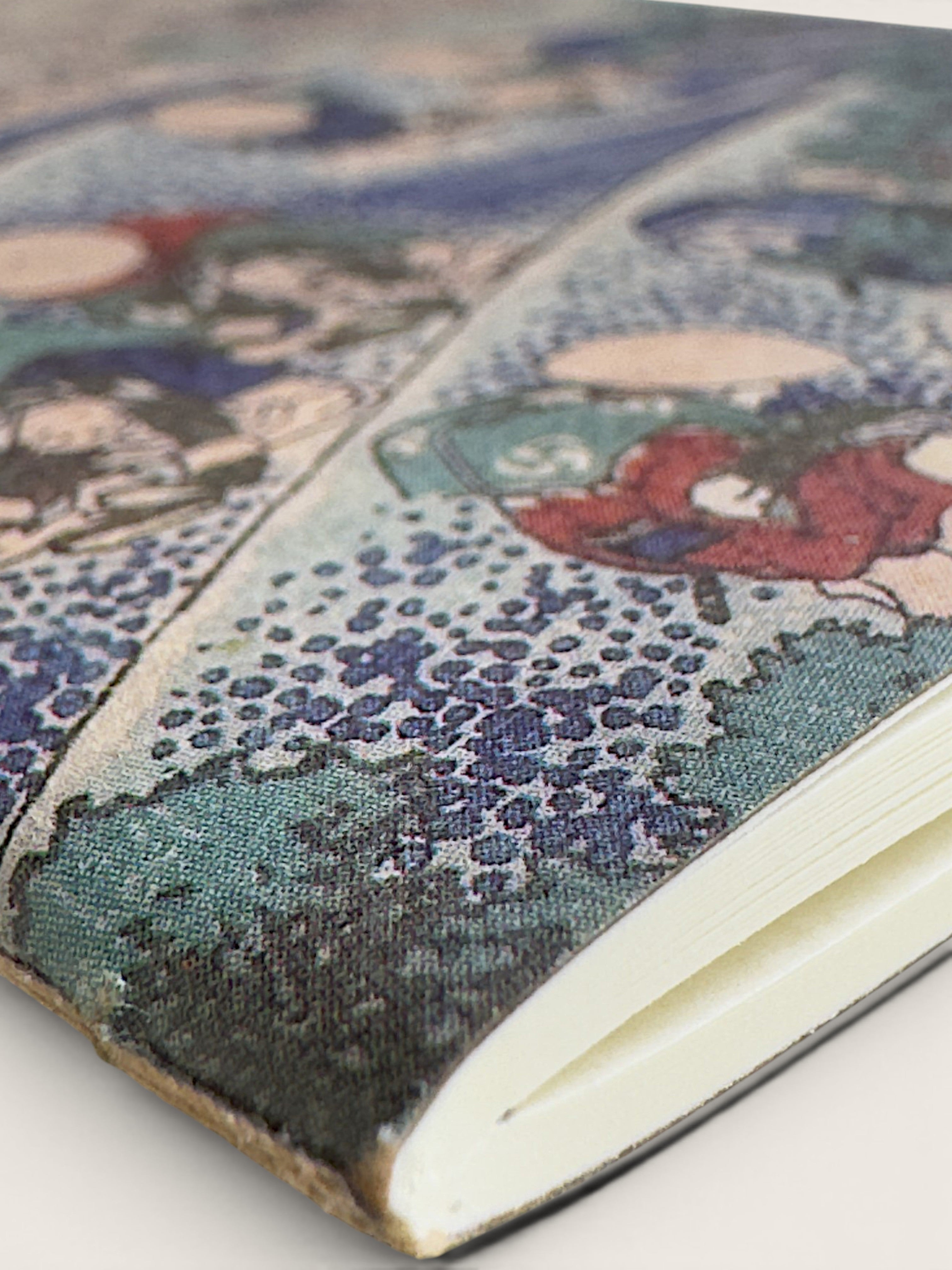 A close-up of a hardcover notebook or journal with a detailed, vintage-style Japanese wave illustration on the cover, showing a textured canvas-like fabric surface and white pages.