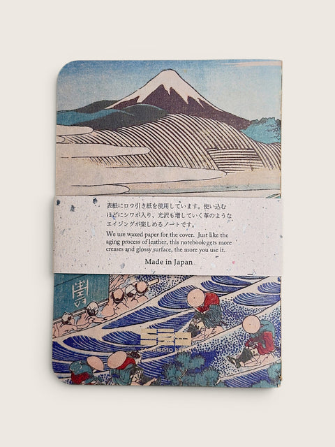 A vintage-style notebook or journal with a Japanese woodblock print cover featuring Mount Fuji and waves, wrapped with a paper band that reads 'Made in Japan' with additional text about wound paper.