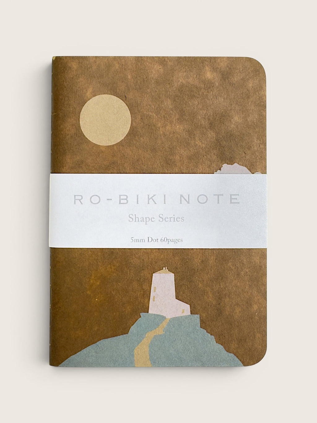A notebook with a textured brown cover featuring a minimalist illustration of a lighthouse, a winding path, and a pale yellow sun. A white paper band across the center reads 'RO-BIKI NOTE Shape Series'.