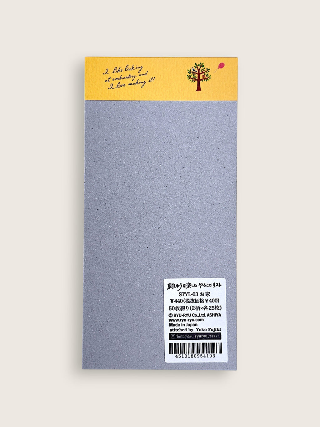A single rectangular notebook or journal cover shown flat against a light warm gray background. The top section is mustard yellow with a small illustrated tree and handwritten-style text, while the main body is a textured light gray.