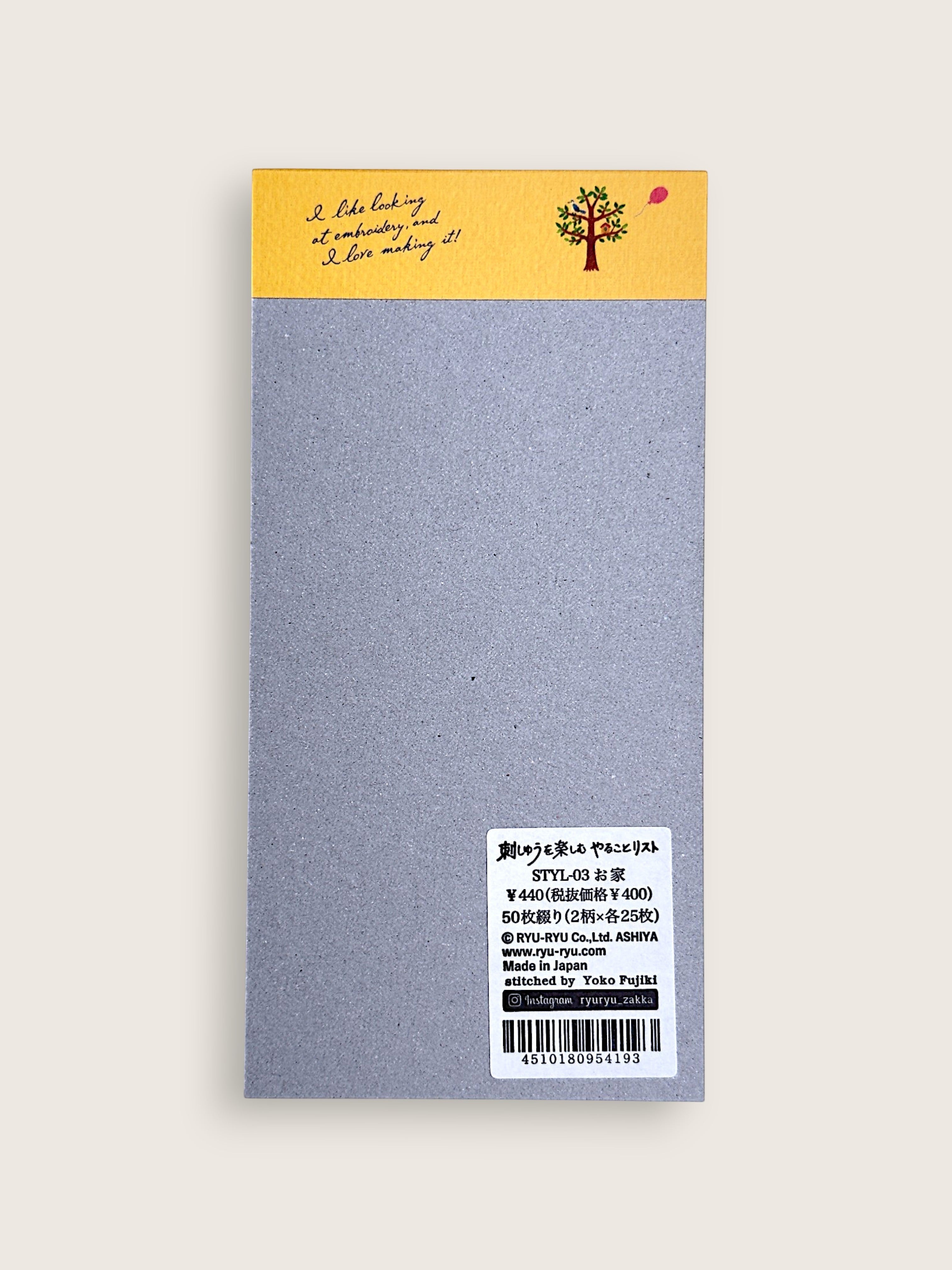 A single rectangular notebook or journal cover shown flat against a light warm gray background. The top section is mustard yellow with a small illustrated tree and handwritten-style text, while the main body is a textured light gray.