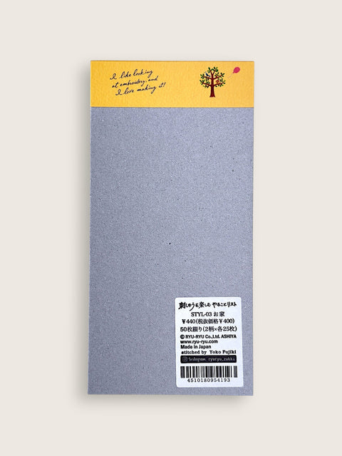 A single rectangular notebook or journal cover shown flat against a light warm gray background. The top section is mustard yellow with a small illustrated tree and handwritten-style text, while the main body is a textured light gray.