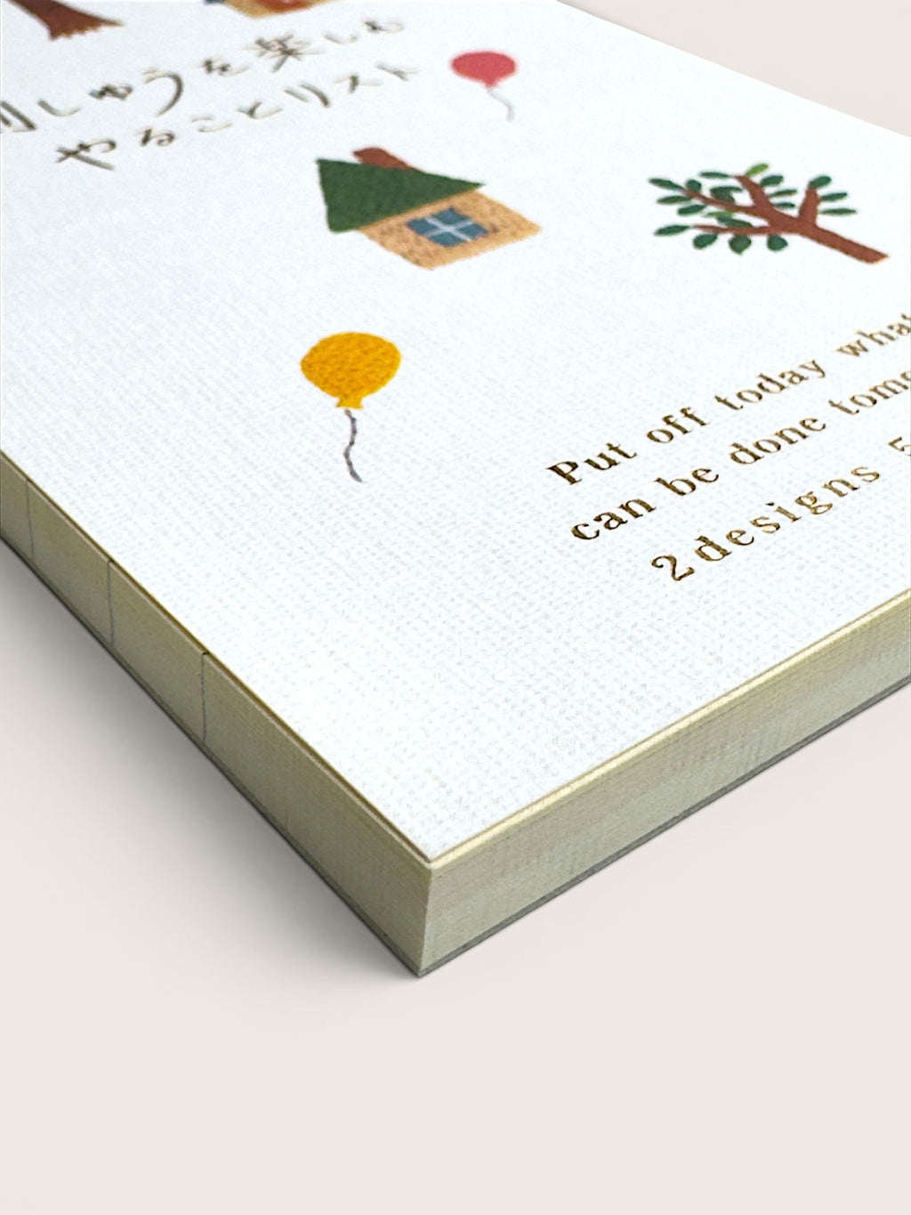 A close-up of a white textured notebook or journal cover with small illustrated drawings, including a house, tree, and balloons, alongside partial printed text on a light beige background.