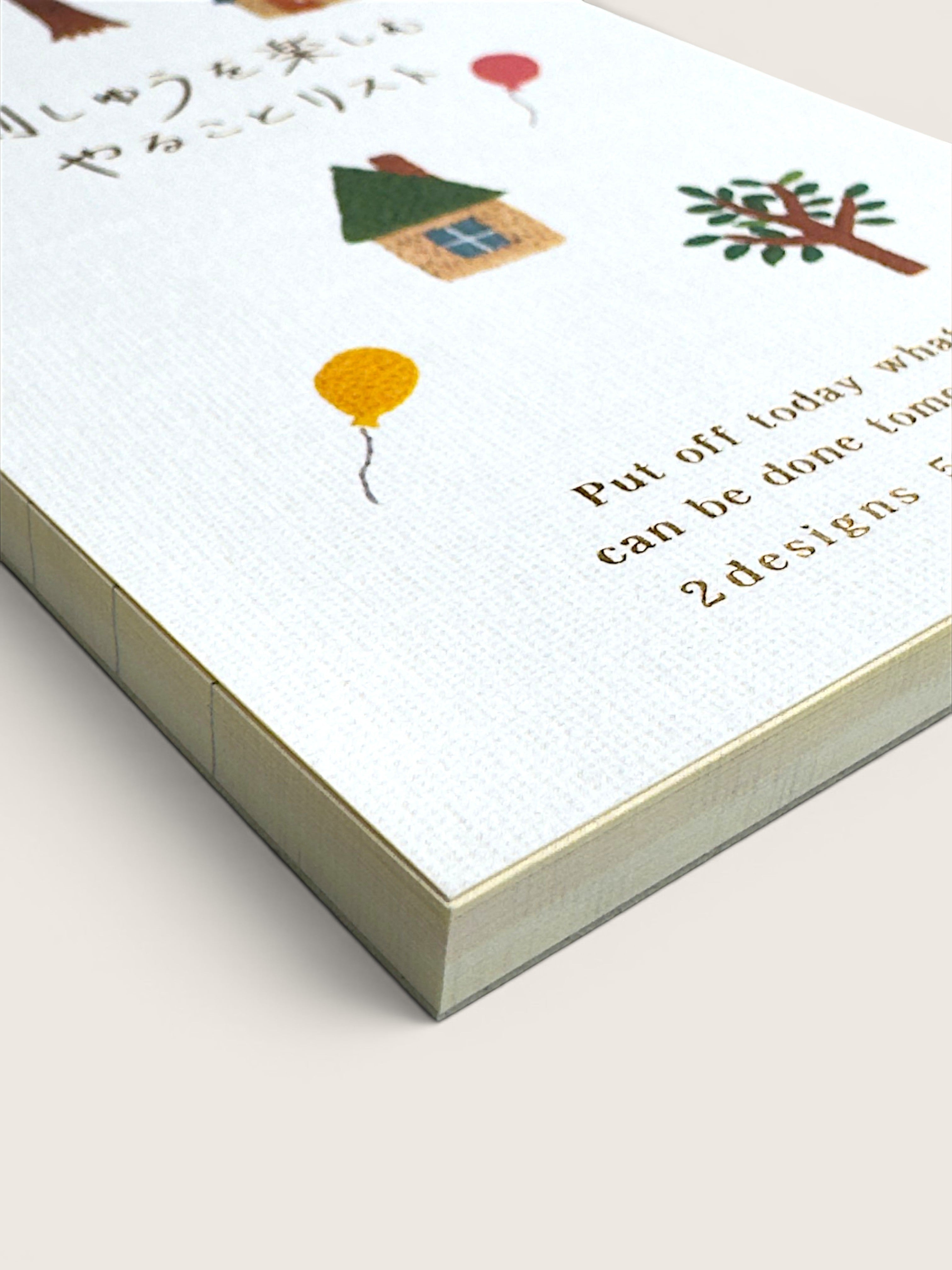 A close-up of a white textured notebook or journal cover with small illustrated drawings, including a house, tree, and balloons, alongside partial printed text on a light beige background.
