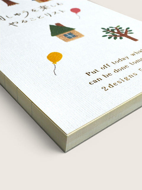 A close-up of a white textured notebook or journal cover with small illustrated drawings, including a house, tree, and balloons, alongside partial printed text on a light beige background.