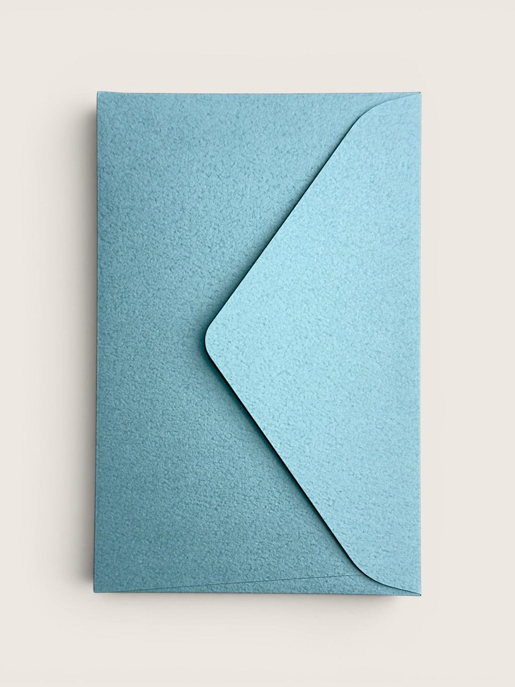 A light blue textured paper envelope with a matching flap, shown flat against a warm off-white background.