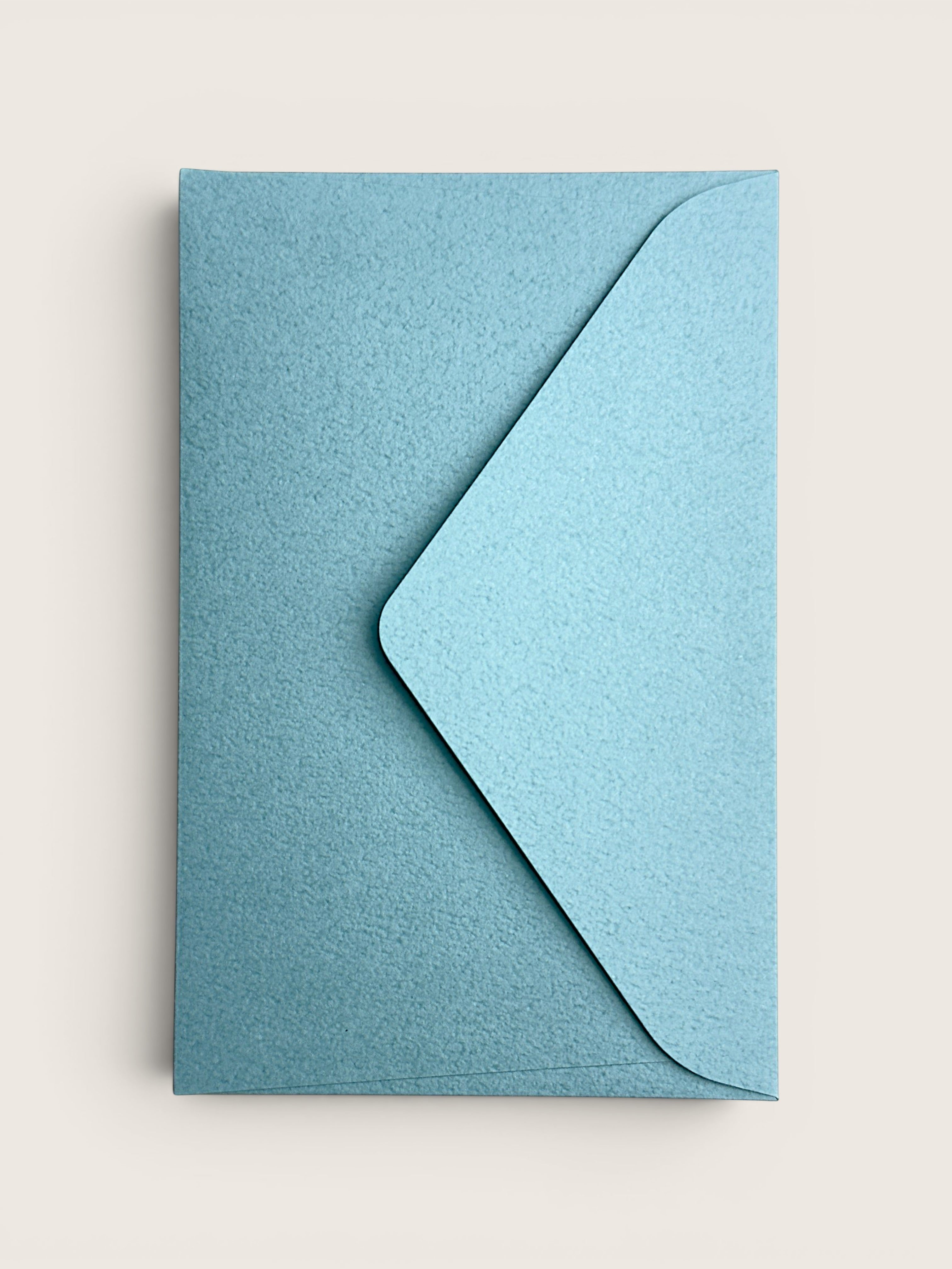 A light blue textured paper envelope with a matching flap, shown flat against a warm off-white background.