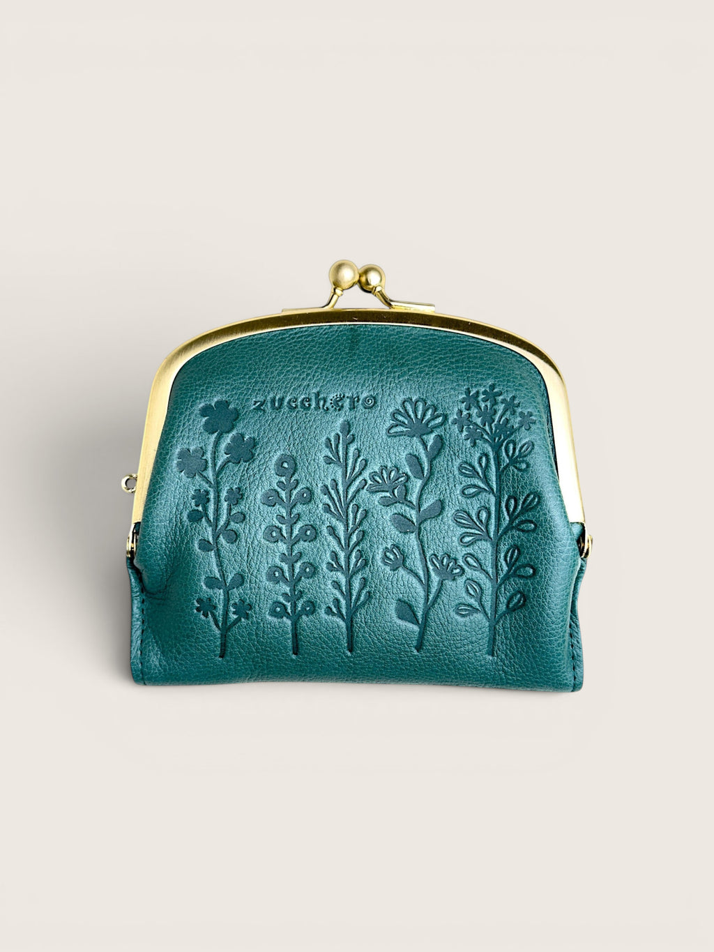 A small teal leather kiss-lock wallet with embossed floral designs and the brand name 'zucchero' on the front, set against a solid light beige background.