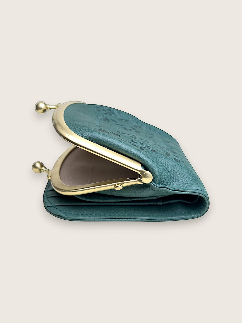 A teal leather coin purse with a gold-tone metal frame and clasp, shown open on a light beige background.