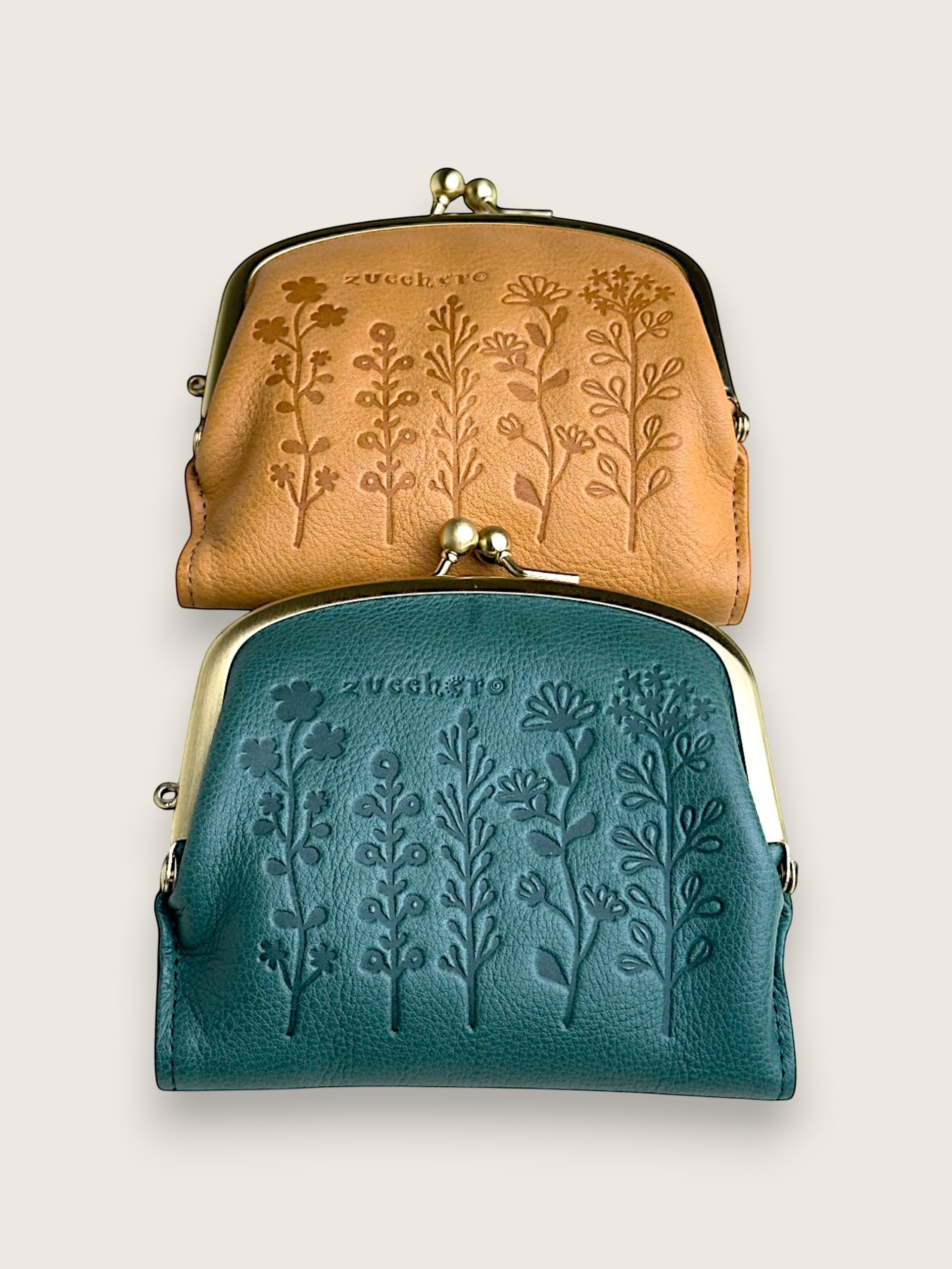Two small kiss-lock leather pouches stacked vertically on a light beige background. The top pouch is tan with embossed floral tree designs, and the bottom pouch is teal with embossed floral tree designs.
