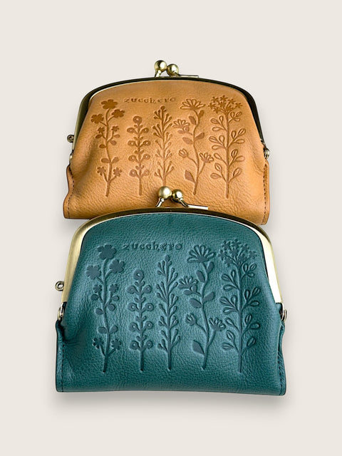 Two small kiss-lock leather pouches stacked vertically on a light beige background. The top pouch is tan with embossed floral tree designs, and the bottom pouch is teal with embossed floral tree designs.