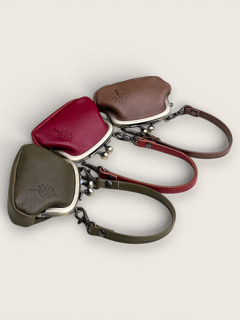Four small leather kiss-lock wristlet pouches with adjustable straps, arranged in a fan shape on a light beige background. The pouches are in olive green, burgundy red, and brown, each with a small embossed logo on the front.