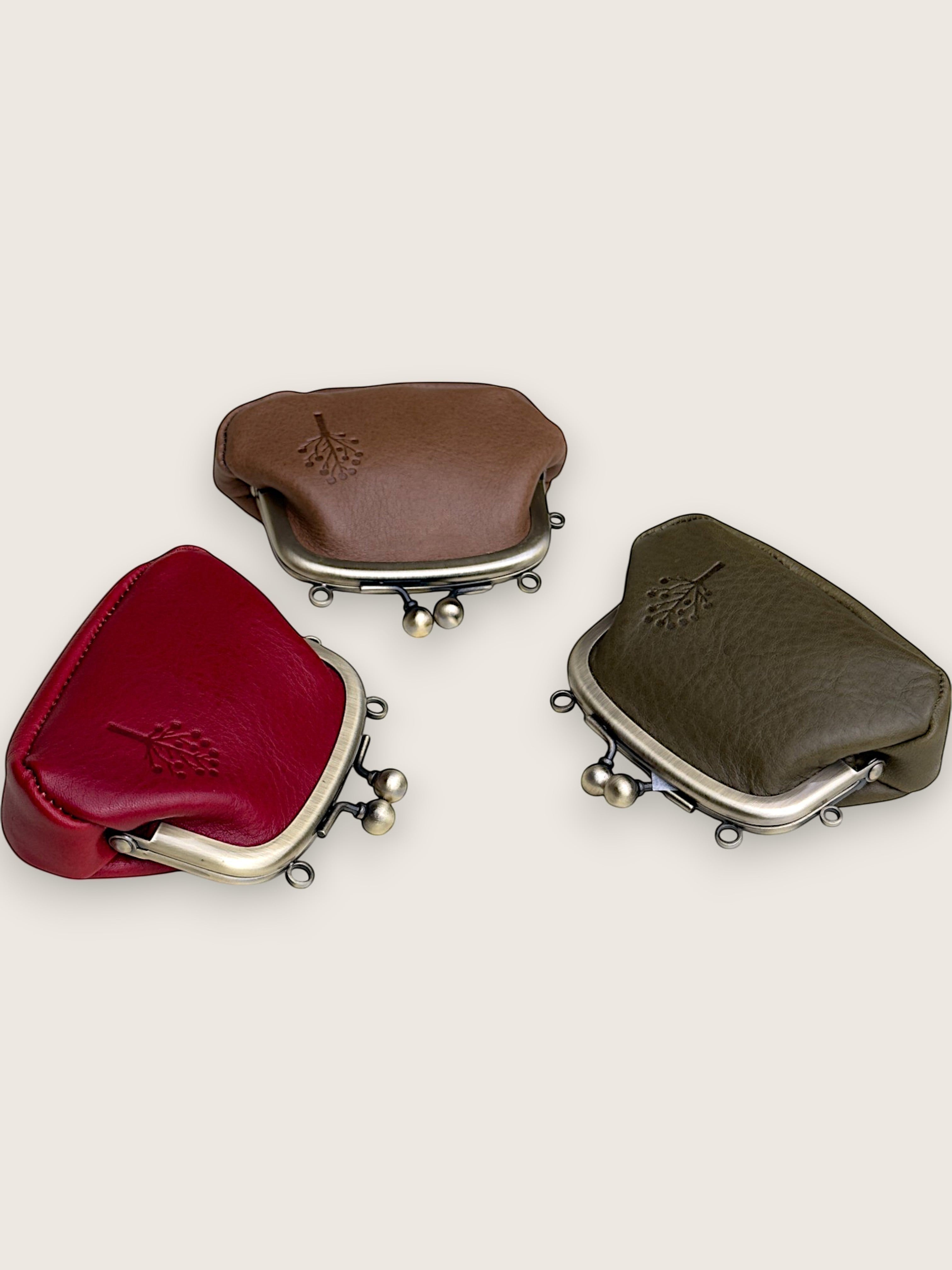 Three small leather kiss-lock coin purses in red, brown, and olive green, arranged on a light beige background.