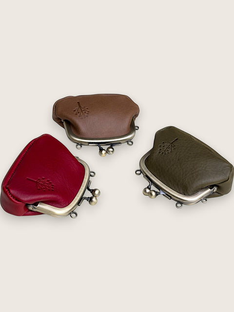 Three small leather kiss-lock coin purses in red, brown, and olive green, arranged on a light beige background.