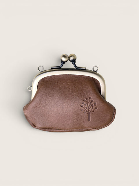 A small brown leather kiss-lock coin purse with a silver-tone metal frame and a debossed tree logo on the front, set against a solid light beige background.