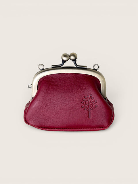 A burgundy faux leather kiss-lock coin purse with a silver-tone metal frame and a debossed tree logo on the front, set against a solid off-white background.