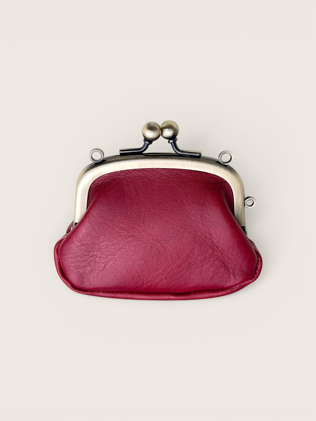 A burgundy faux leather kiss-lock coin purse with a silver-toned metal frame and black spring clasp, shown from a top-down view on a light beige background.
