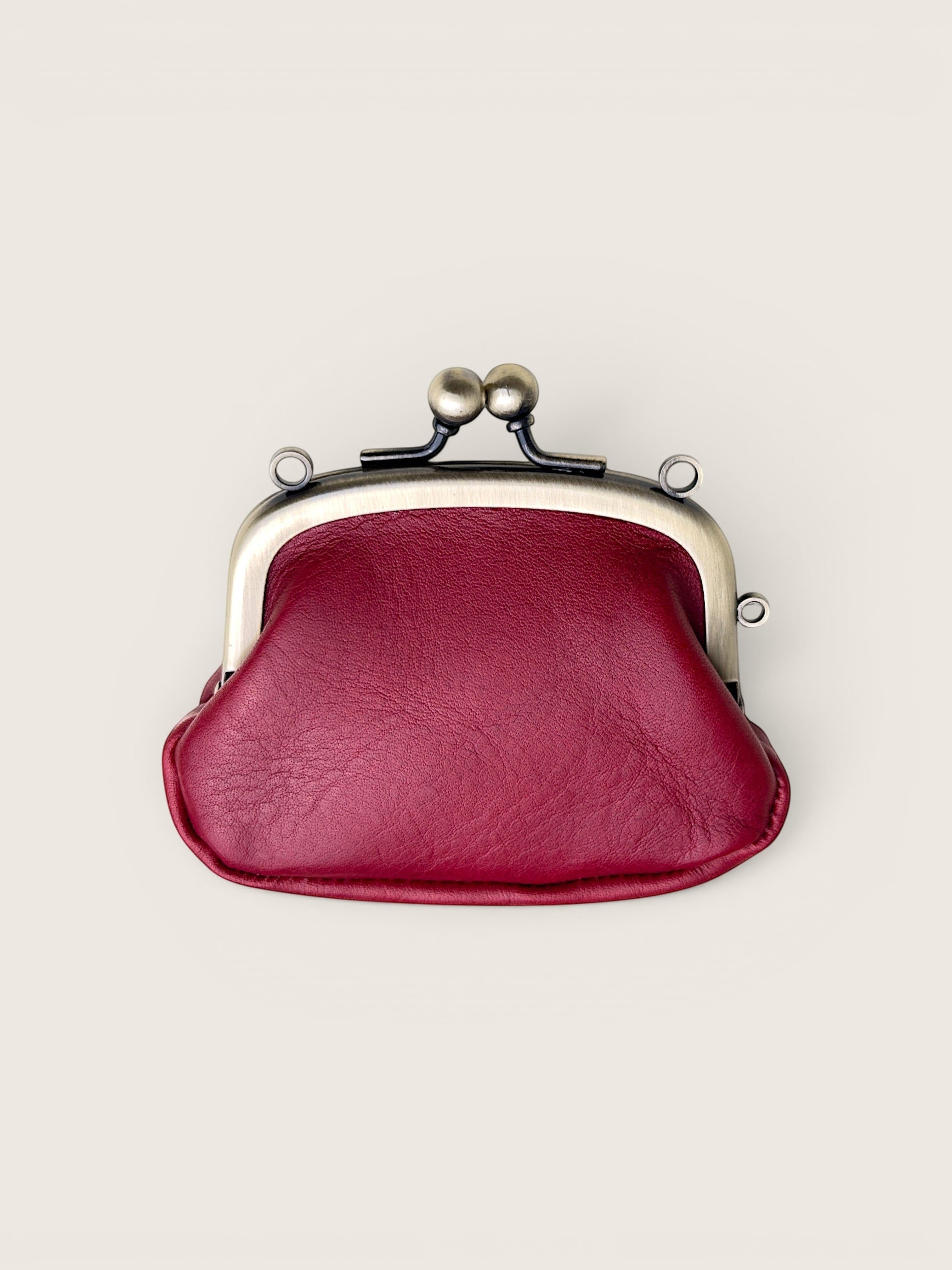 A burgundy faux leather kiss-lock coin purse with a silver-toned metal frame and black spring clasp, shown from a top-down view on a light beige background.