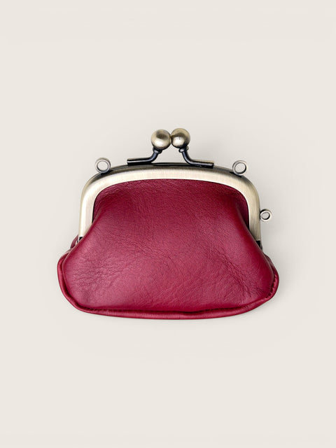 A burgundy faux leather kiss-lock coin purse with a silver-toned metal frame and black spring clasp, shown from a top-down view on a light beige background.