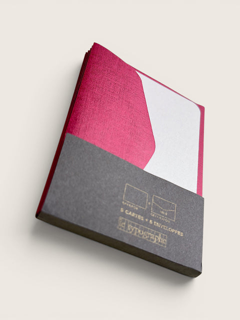 A stack of pink and white textured envelopes in a clear plastic sleeve with a dark gray paper band at the bottom, photographed on a light beige background.