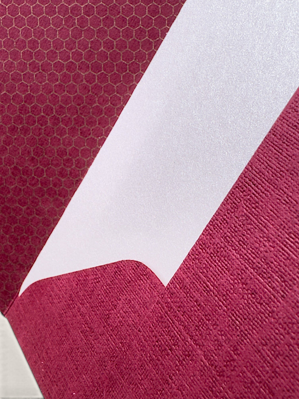 A close-up of a folded fabric or paper product showing two sides: one side has a magenta-pink honeycomb pattern, and the other side is a solid white textured surface.