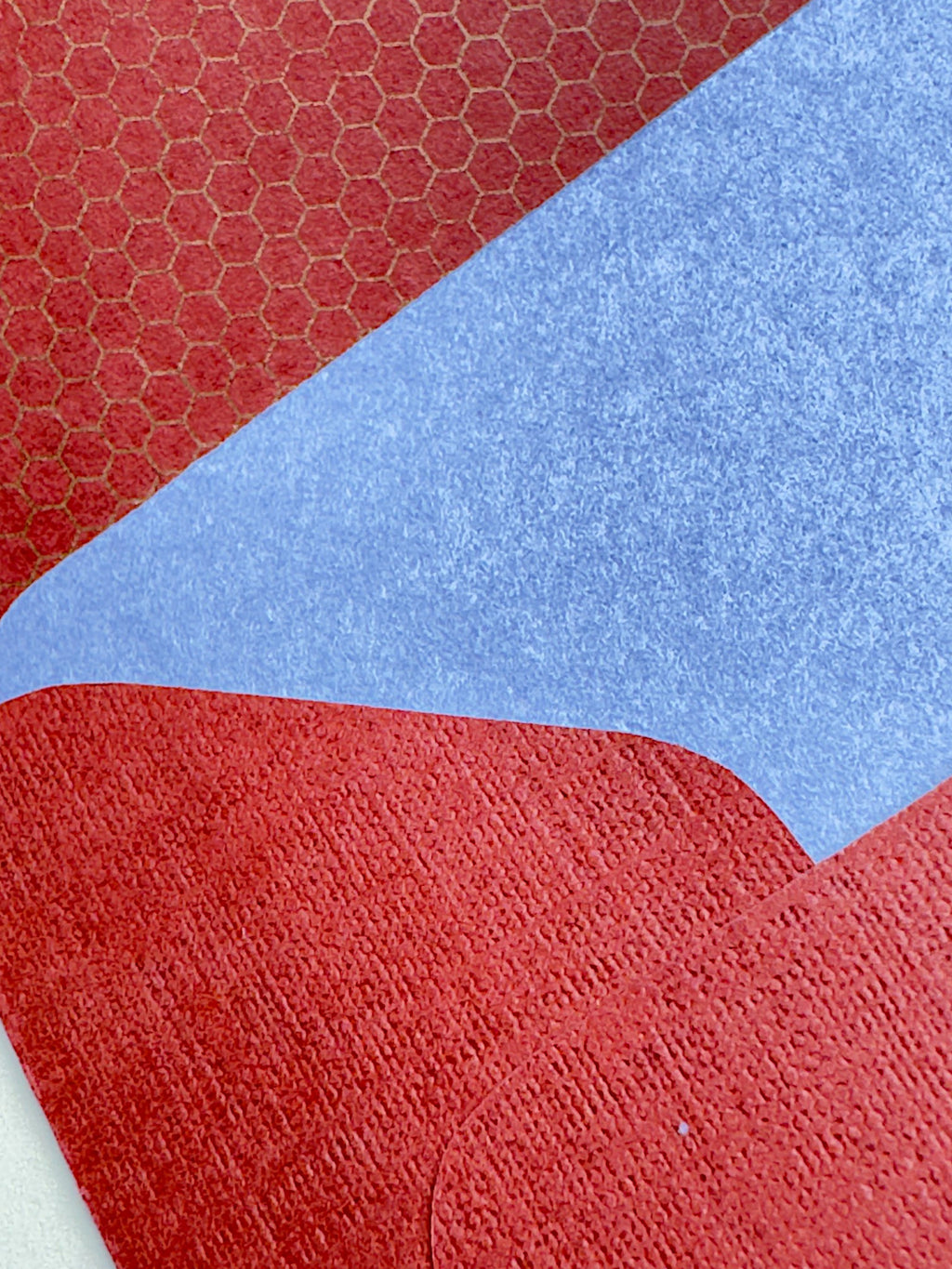 A close-up of a textured surface with large color-blocked sections: red with a subtle honeycomb pattern in the top-left, a broad light blue section across the center-right, and red in the bottom and lower-left areas.