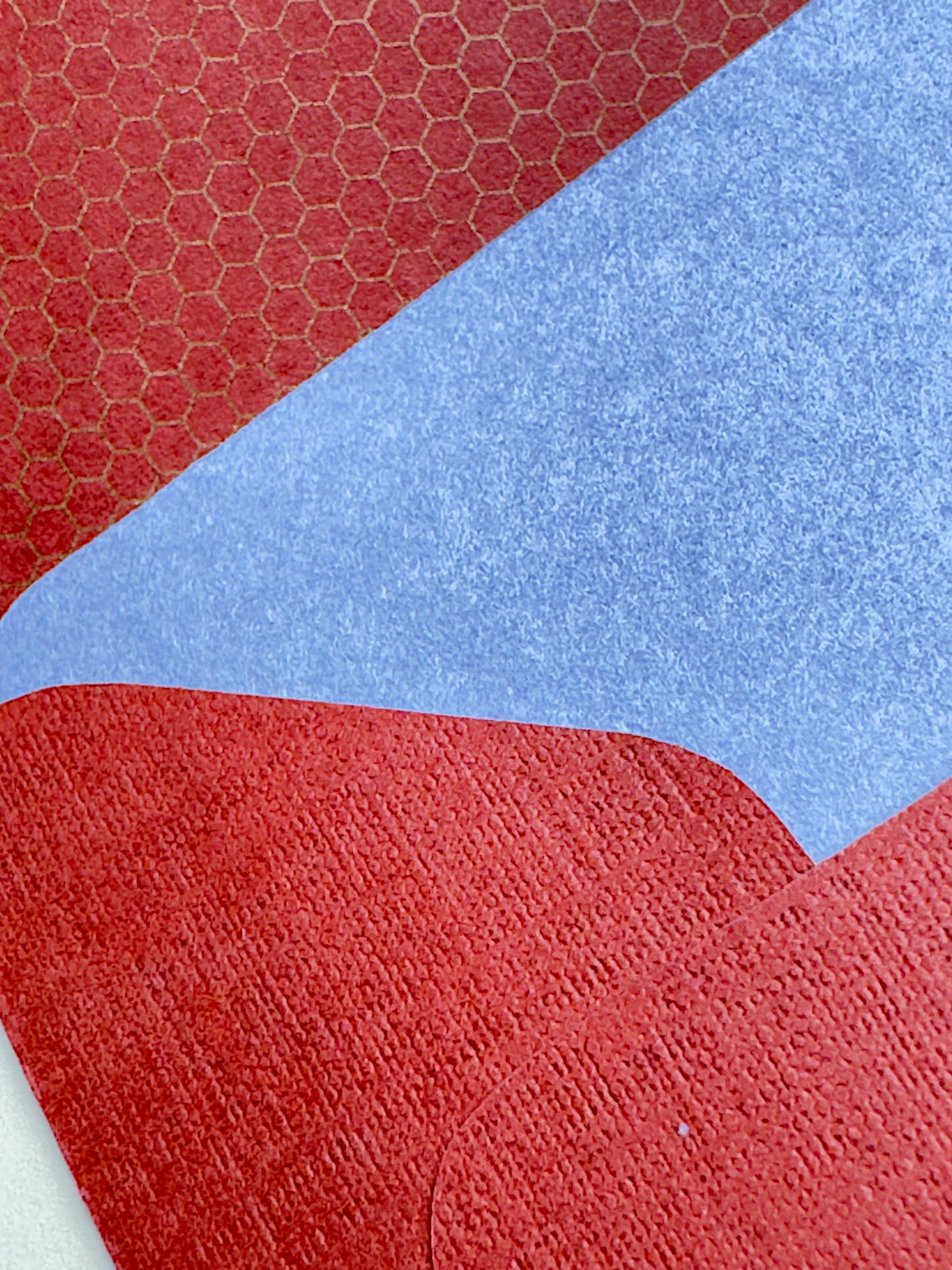 A close-up of a textured surface with large color-blocked sections: red with a subtle honeycomb pattern in the top-left, a broad light blue section across the center-right, and red in the bottom and lower-left areas.