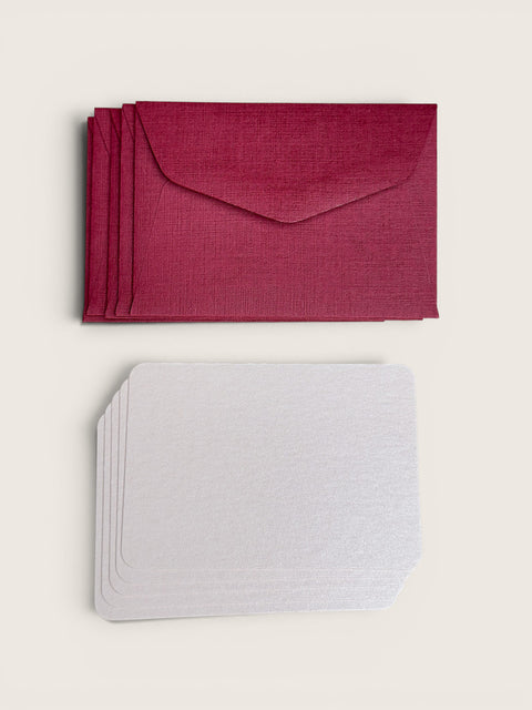A stack of textured envelope-style cards in a deep magenta color, shown above a matching stack of plain white cards, all on a light beige background.