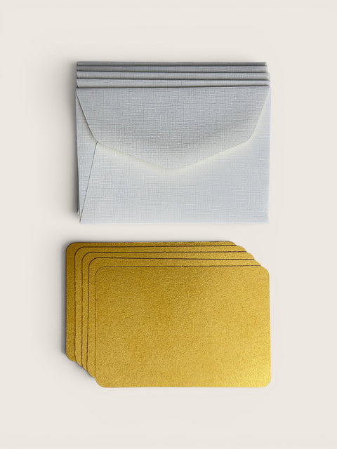 A set of textured white envelopes stacked on top of matching gold metallic cards, arranged neatly on a light beige background.