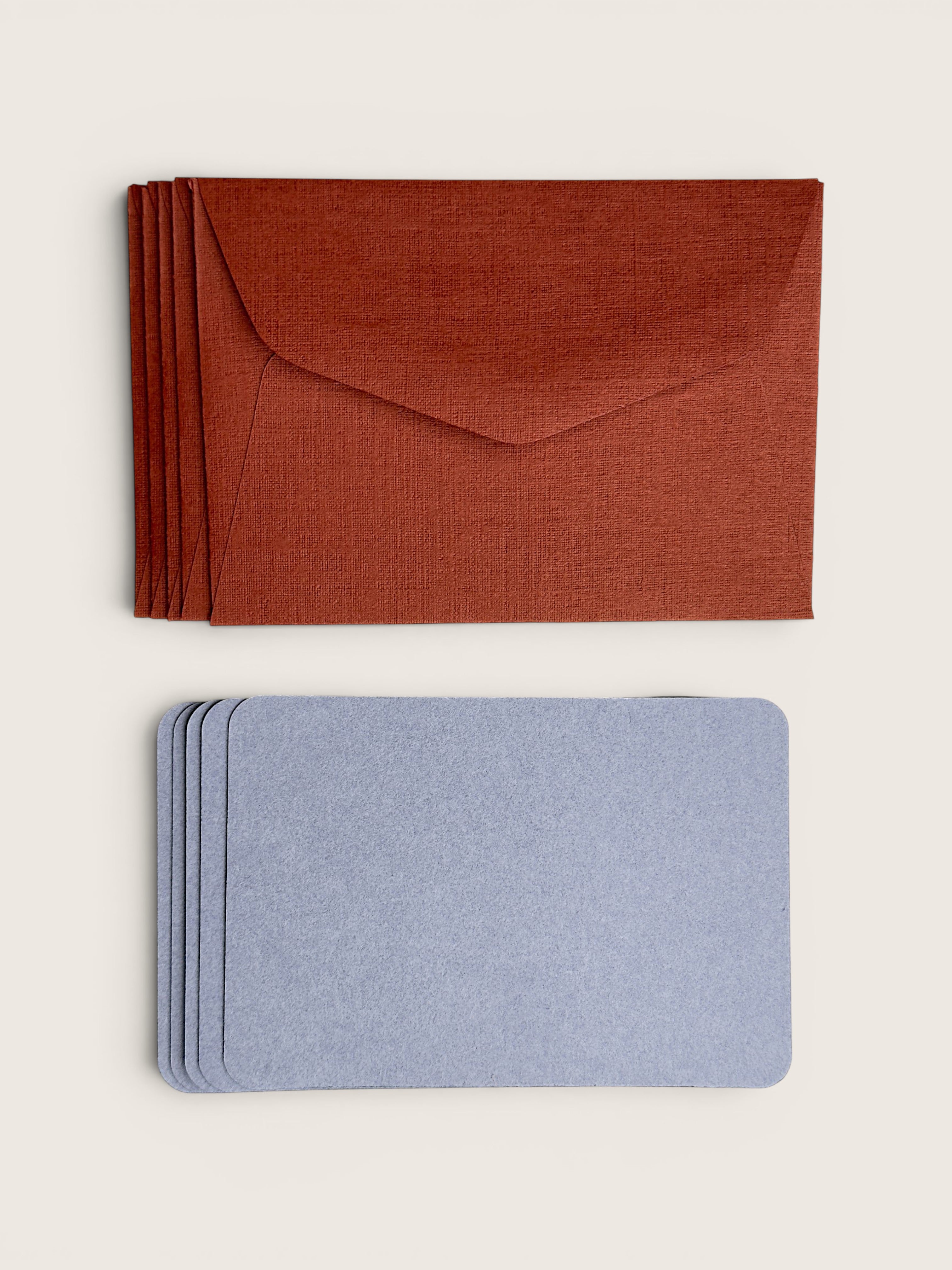 A stack of rust-orange textured envelopes on top and a stack of matching light blue textured cards or inserts below, arranged on a plain light beige background.