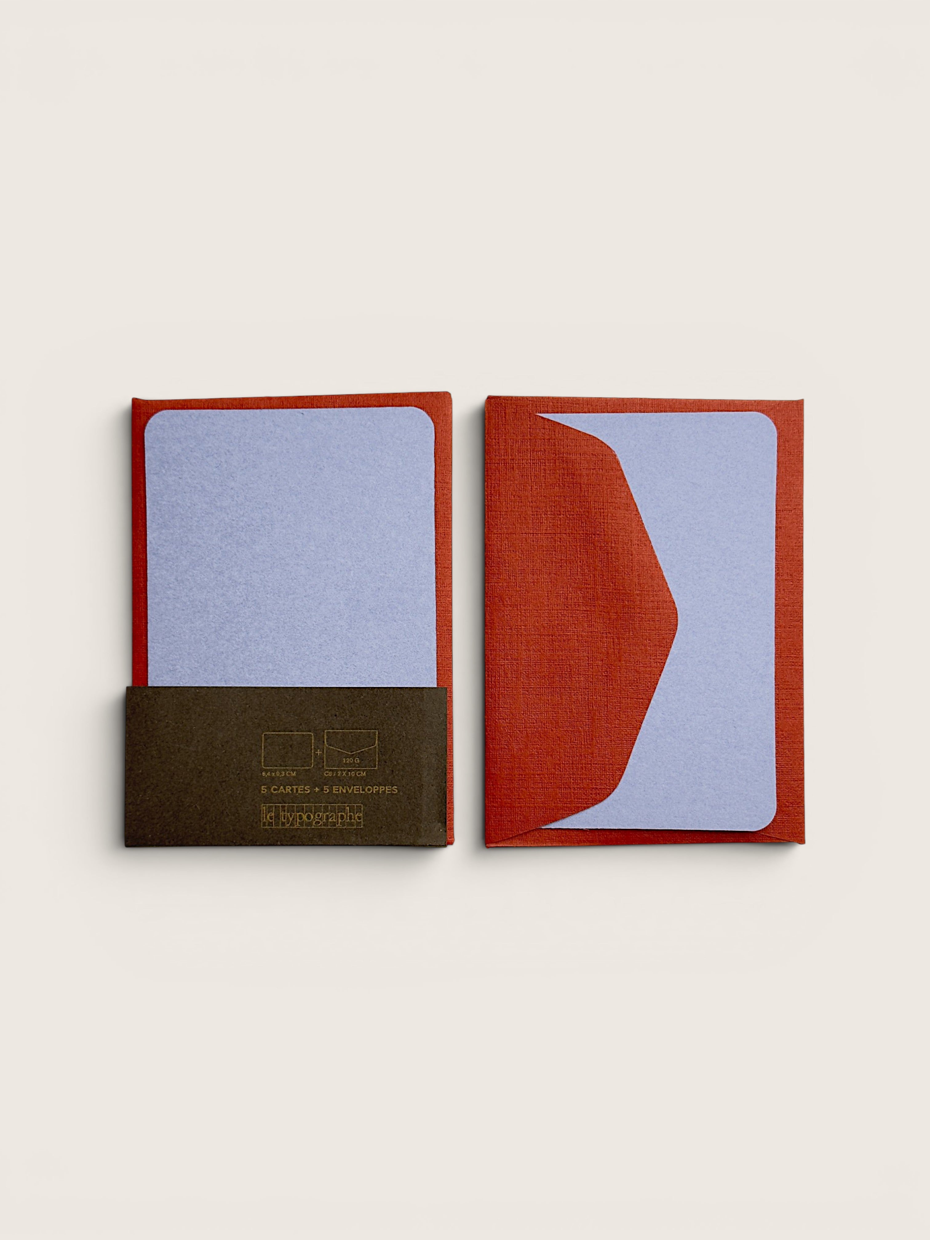 Two small square notebooks or cards with textured fabric covers are shown on a plain light beige background. One cover is dark brown with gold text, and the other is rust red with a large pale lavender abstract shape.