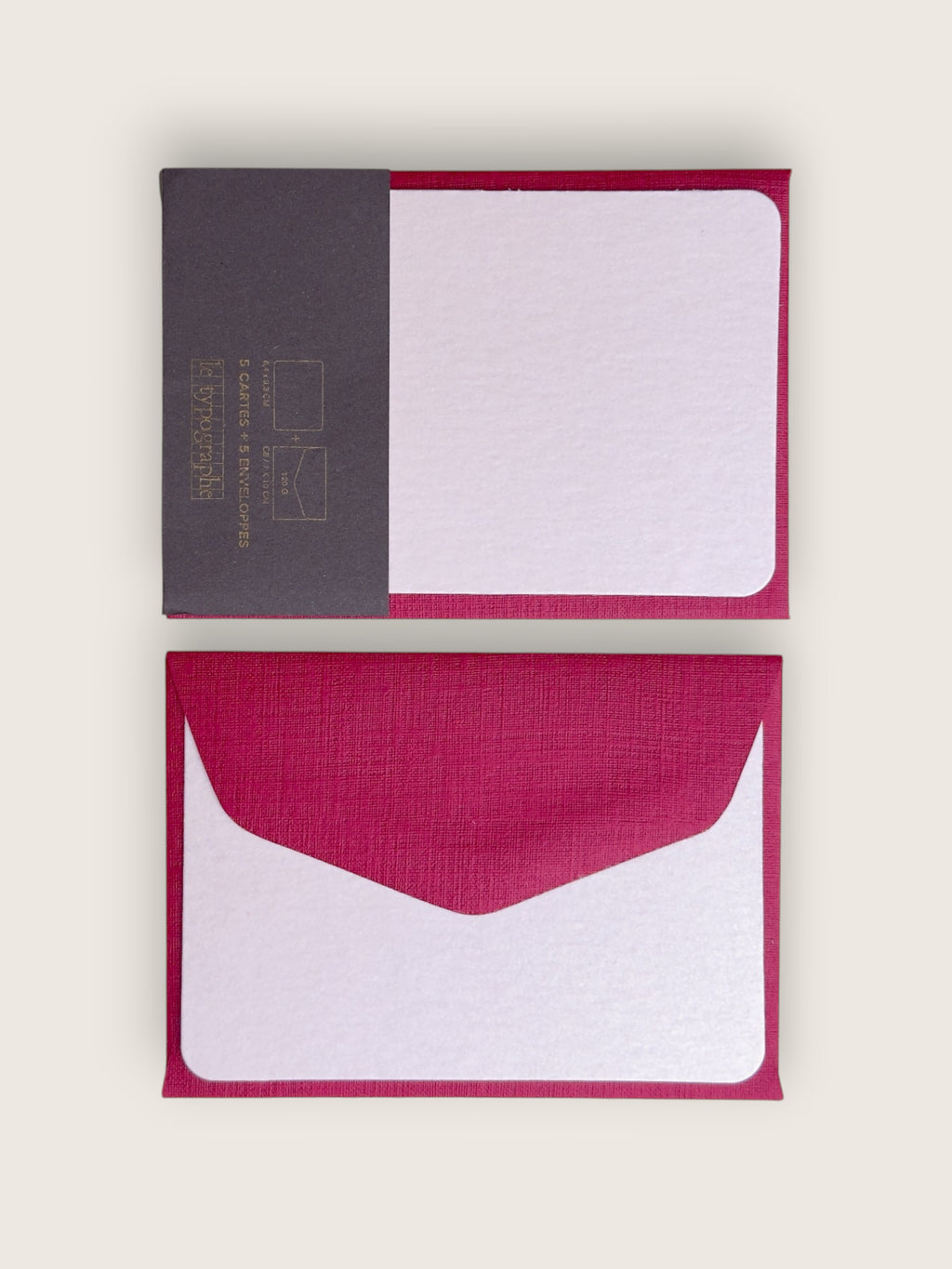A set of minimalist stationery cards and envelopes on a light beige background. The set includes a closed card with a dark gray textured left panel and a magenta-pink right border, and an open matching envelope below it showing a white textured center with a magenta-pink border.